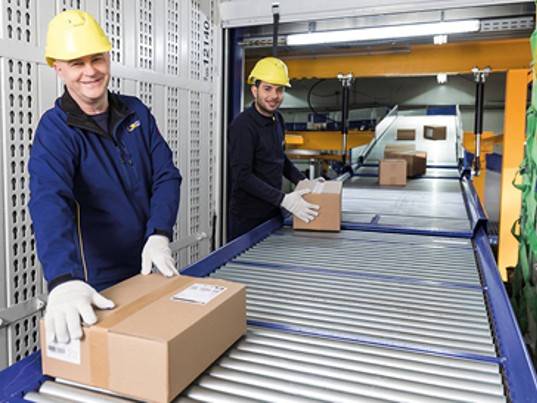 Employés souriants GLS France trient colis tapis roulant