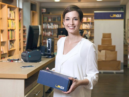 Femme souriant tient colis GLS France dans bureau dépôt